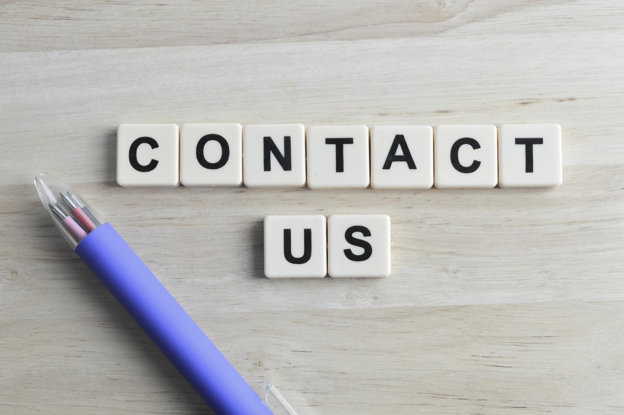 Square letters with text CONTACT US over wooden background.